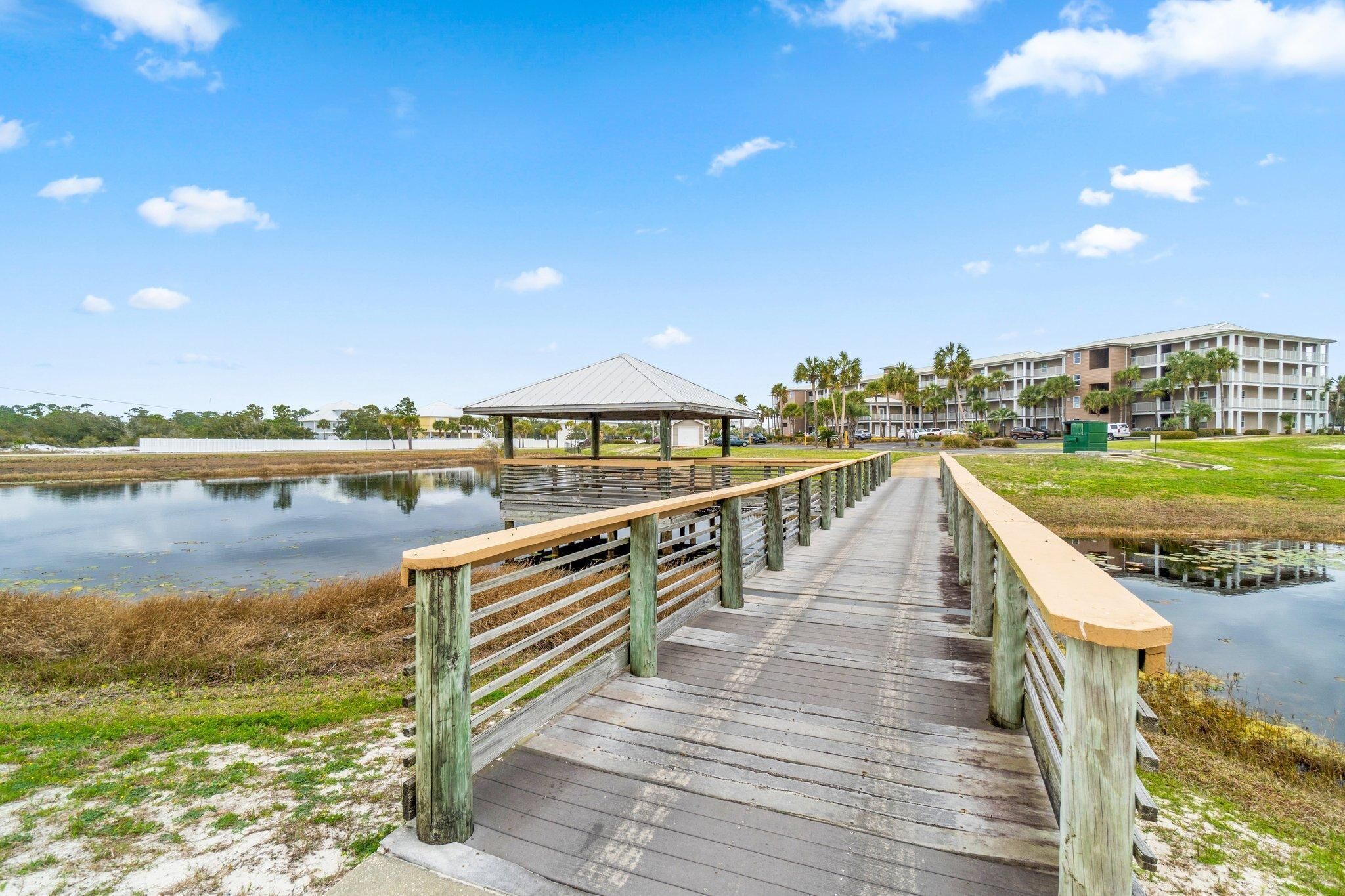 A wooden boardwalk leading to a gazebo over a calm body of water, with a building in the background.