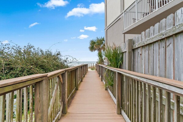 A wooden boardwalk leading to a building with a balcony. - Grand Caribbean West 303 (Pensacola)