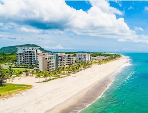 A beachfront hotel with multiple buildings, a sandy beach, and clear turquoise waters. - Oceanfront 4BR Suite on the Beach Playa Caracol Beach Club and Resort (Chame)