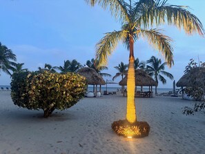 Een strand met palmbomen, rieten parasols en ligbedden.