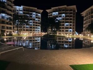 Een nachtzicht van een hotel met meerdere gebouwen, een reflectiebad en verlichte balkons.