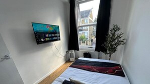 Een slaapkamer met een bed, een aan de muur bevestigde televisie, een radiator en een raam met gordijnen.