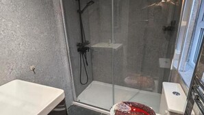 Een douche met glazen deur, een witte wastafel en een toilet.