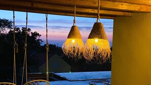 Een buitenterras met een houten tafel en stoelen, twee hanglampen en uitzicht op de lucht.
