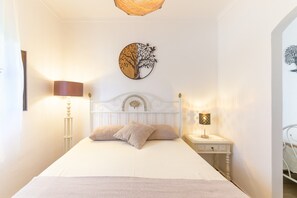 Una cama con cabecera blanca, dos almohadas, una mesita de noche con lámpara y una obra de arte en la pared.