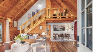 A spacious loft with a wooden staircase, a dining area, and a cozy seating area with a fireplace. - Romantic Mtn Spa Retreat - Views • Hot Tub • Sauna • Fire Pit  • Cold Plunge (Gatlinburg)