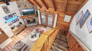 A wooden interior with a fireplace, stone wall, and a staircase. - Romantic Mtn Spa Retreat - Views • Hot Tub • Sauna • Fire Pit  • Cold Plunge (Gatlinburg)