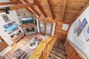 A wooden interior with a fireplace, stone wall, and a staircase. - Romantic Mtn Spa Retreat - Views • Hot Tub • Sauna • Fire Pit  • Cold Plunge (Gatlinburg)
