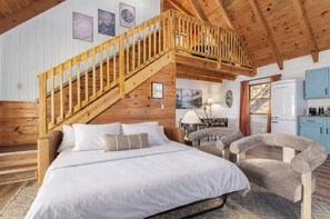 Ein Schlafzimmer mit einer Holztreppe, einem Bett, einem Schreibtisch und einer Küchenzeile.