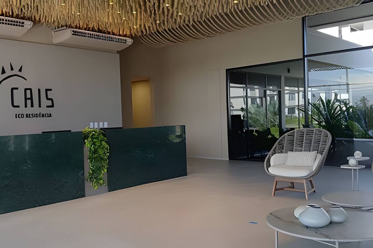 Un área de recepción con diseño moderno, que incluye un mostrador de recepción, una silla de mimbre y un muro de cristal con vistas al exterior.