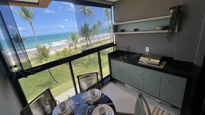 Une cuisine moderne avec vue sur la plage, un coin repas avec une table dressée pour quatre personnes et une grande fenêtre donnant sur l’océan.