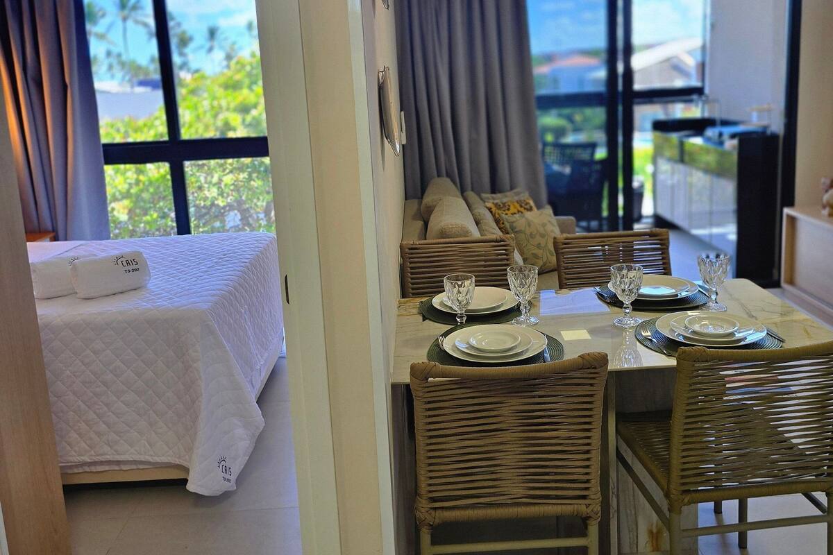 Habitación de hotel con cama, zona de comedor con mesa para dos y vista al exterior.