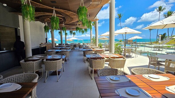 Un espace extérieur aménagé pour les repas, avec des meubles en osier, des parasols et une vue sur l’océan.