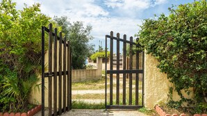 A gated entrance with a concrete wall and a metal gate, surrounded by greenery. - Villa Terri – Beachfront Retreat on Solanas Beach (Solanas)