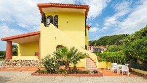 A yellow building with a red roof, a staircase, and a patio area with chairs. - Villa Terri – Beachfront Retreat on Solanas Beach (Solanas)