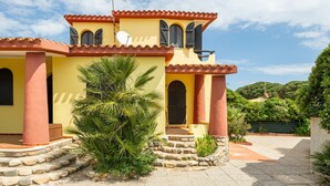 A yellow building with a red roof, a satellite dish, and a stone staircase leading to the entrance. - Villa Terri – Beachfront Retreat on Solanas Beach (Solanas)