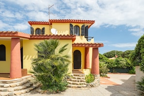 A yellow building with a red roof, a satellite dish, and a stone staircase leading to the entrance.