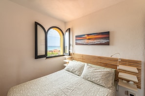 A bedroom with a bed, a window with a view, a painting, and a bedside table.