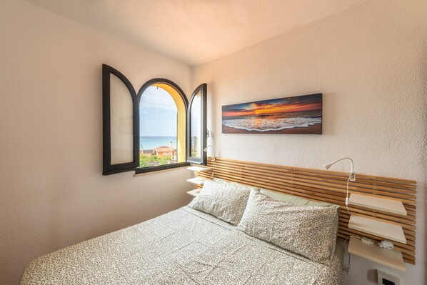 A bedroom with a bed, a window with a view, a painting, and a bedside table.