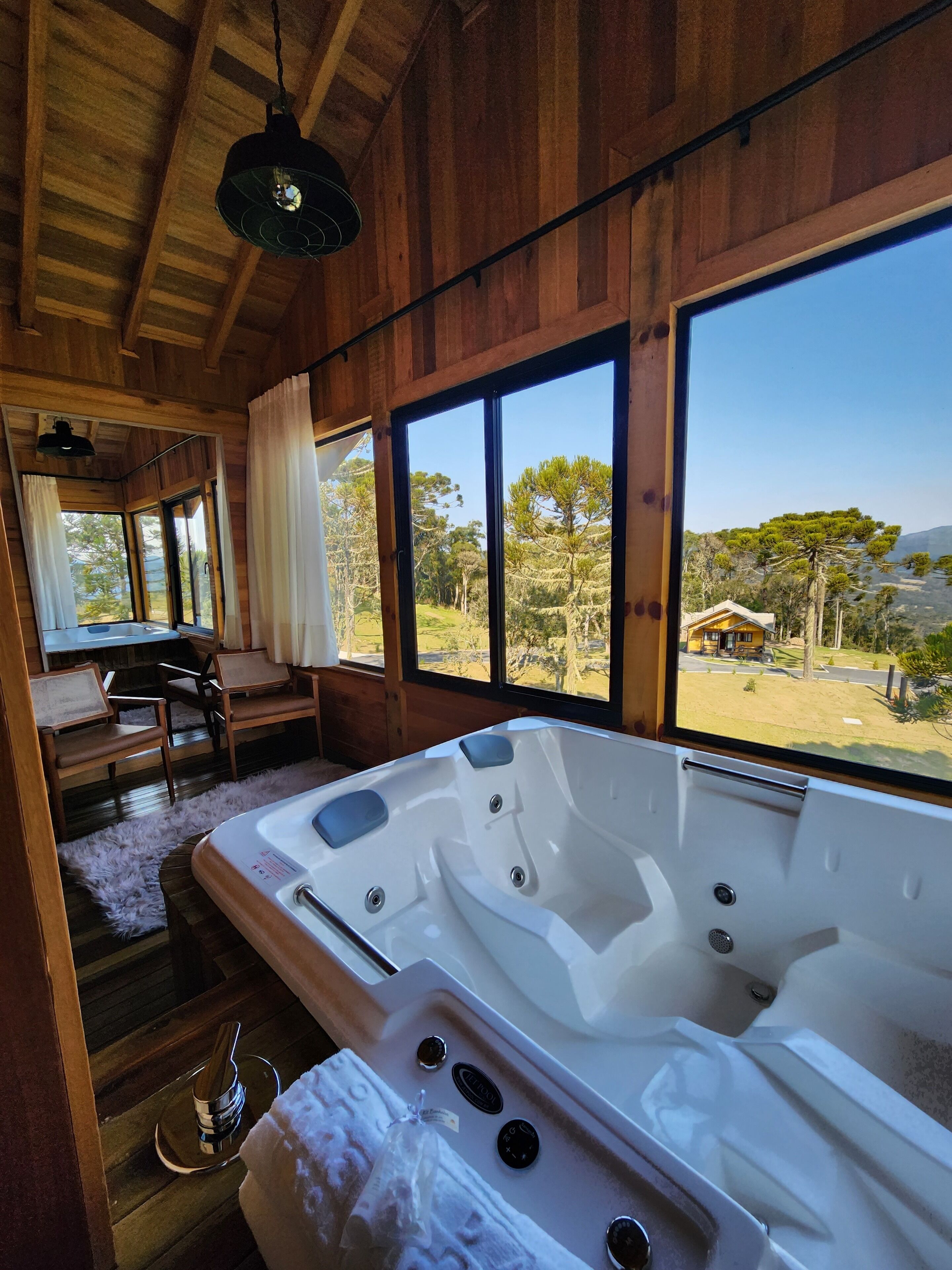 A wooden cabin interior with a large bathtub, a dining area, and a view of the outdoors.