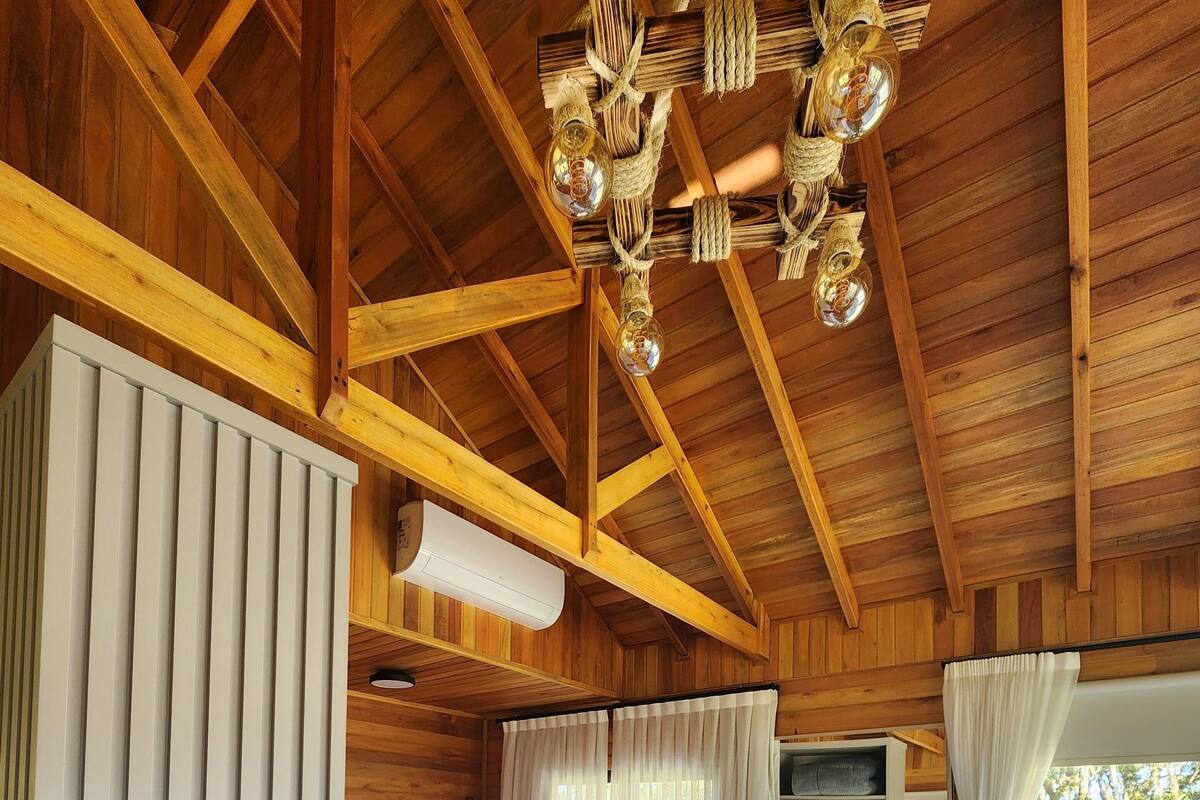A wooden cabin bedroom with two beds, a chandelier, an air conditioning unit, and a view of the outdoors.