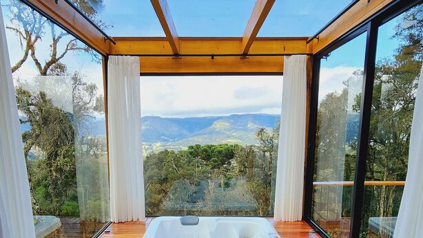 Une terrasse en bois avec un jacuzzi, de grandes fenêtres et une vue sur le paysage.