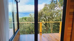 Une pièce dotée d’une grande porte-fenêtre coulissante qui donne sur une terrasse en bois offrant une vue sur un paysage boisé.