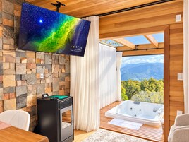 A modern room with a stone wall, a flat-screen TV, a fireplace, a hot tub, and a view of mountains.