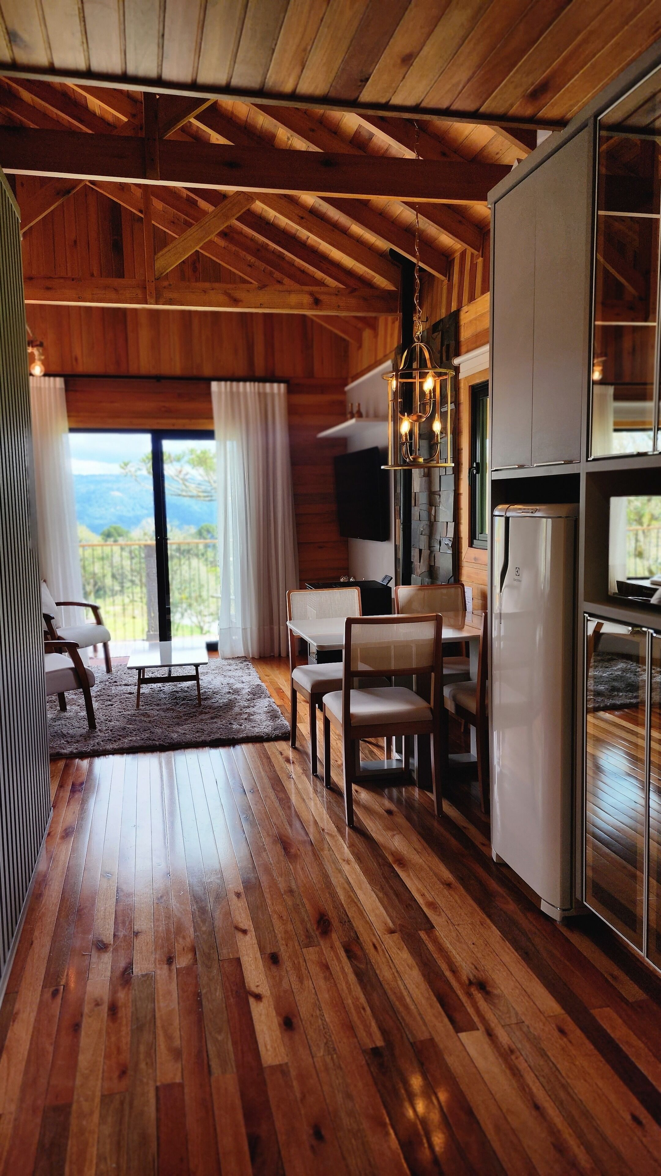 A wooden interior with a dining area, kitchen, and large windows.