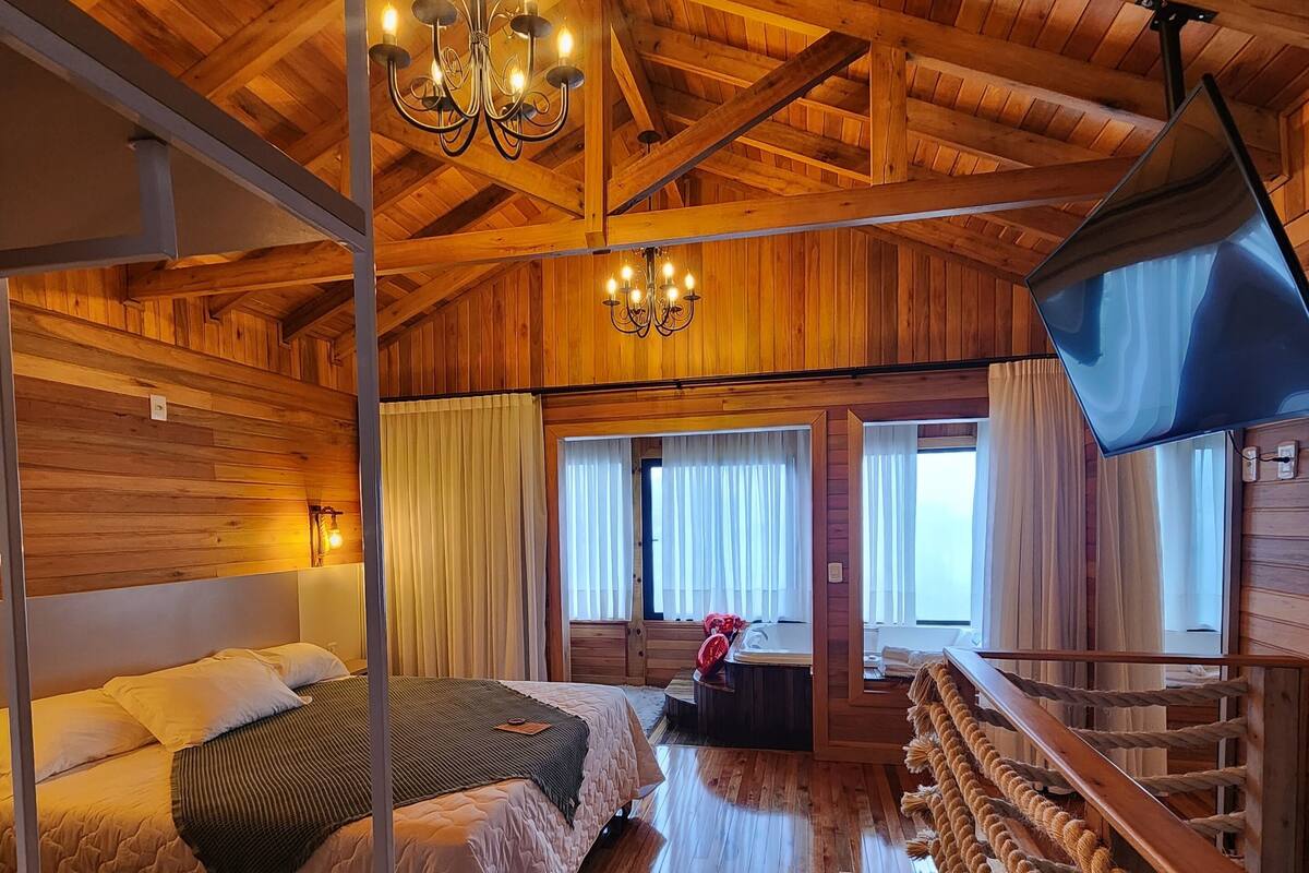A wooden cabin interior with a bunk bed, a chandelier, a television, and a rope ladder.