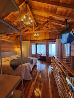 A wooden cabin interior with a bunk bed, a chandelier, a television, and a rope ladder.