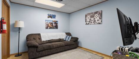A room with a brown sofa, a fire extinguisher, a lamp, a television, and a wall with a poster.