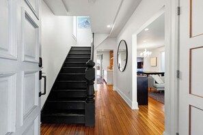 Un escalier menant à un deuxième étage, un coin repas agrémenté d’un lustre, et un grand miroir au mur.