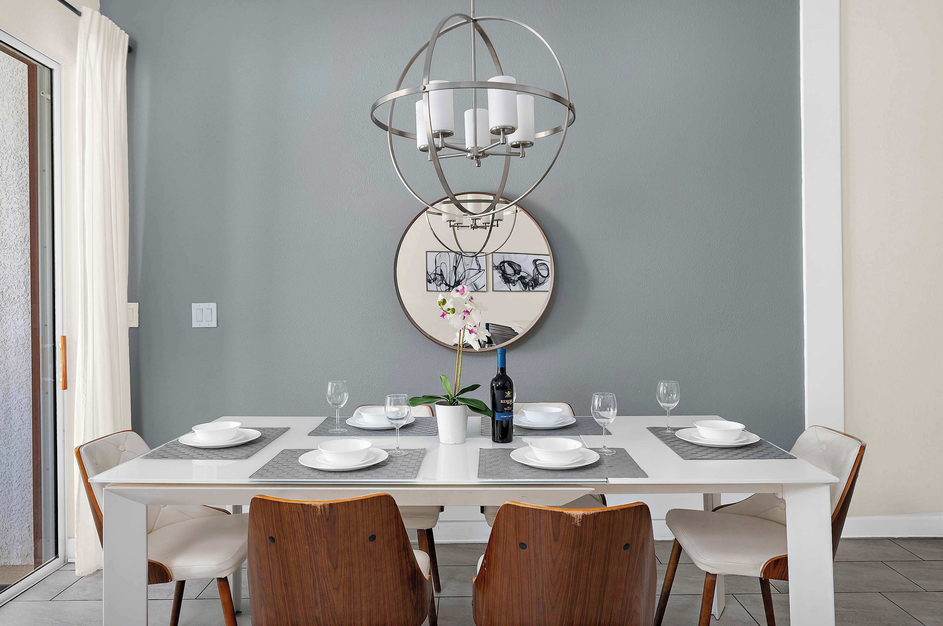 Un comedor con una mesa blanca dispuesta para cuatro personas, una lámpara moderna de araña y una obra de arte colgada en la pared.