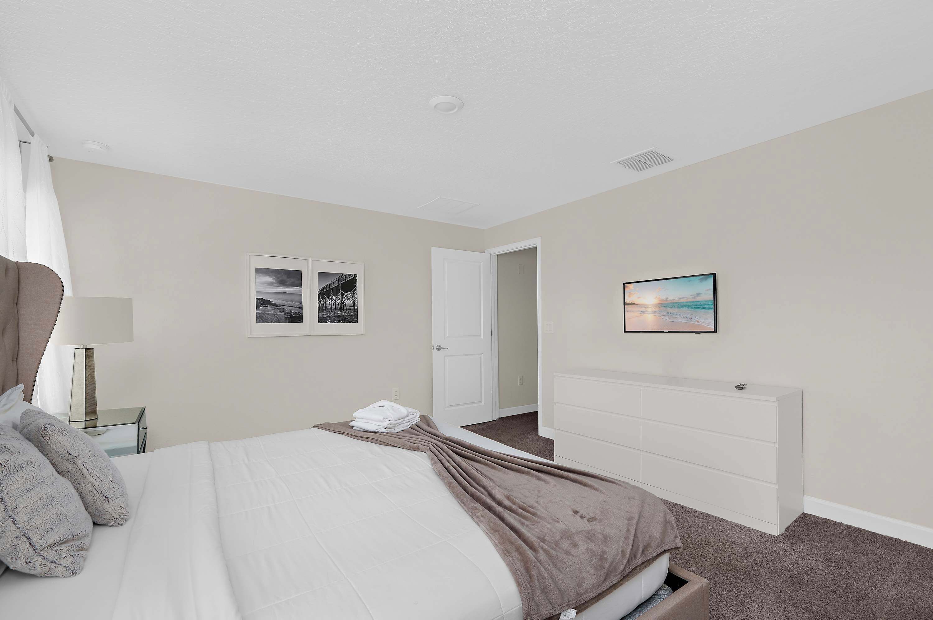 A bedroom with a bed, bedside table, lamp, and a dresser.