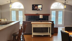 Een ruime woonkamer met een open haard, houten meubels en een aan de muur bevestigde televisie.