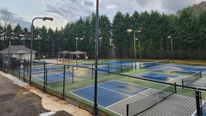 Een tennisbaan met een hek, straatlampen en een prieel op de achtergrond.