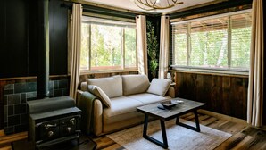 Un salon chaleureux avec une cheminée, un canapé, une table basse et de grandes fenêtres avec des rideaux.
