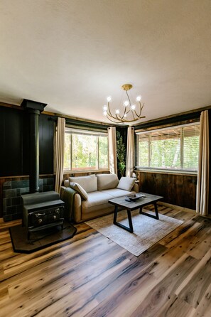 A cozy living room with a fireplace, a sofa, a coffee table, and large windows with curtains.