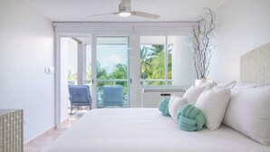 Een slaapkamer met een groot bed, een plafondventilator en uitzicht op palmbomen door de glazen deuren.