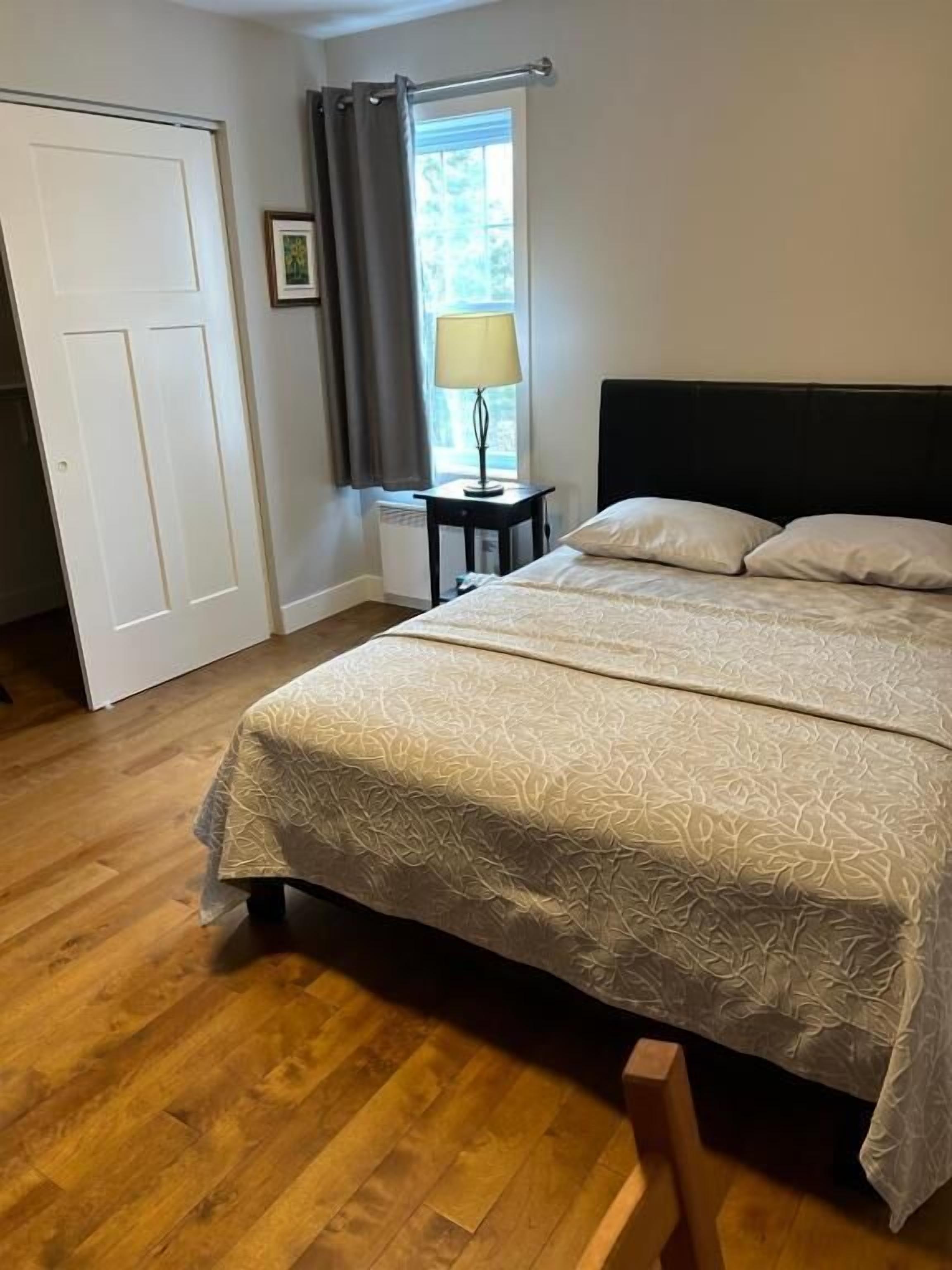 Un dormitorio con cama, mesita de noche, ventana con cortinas y puerta.