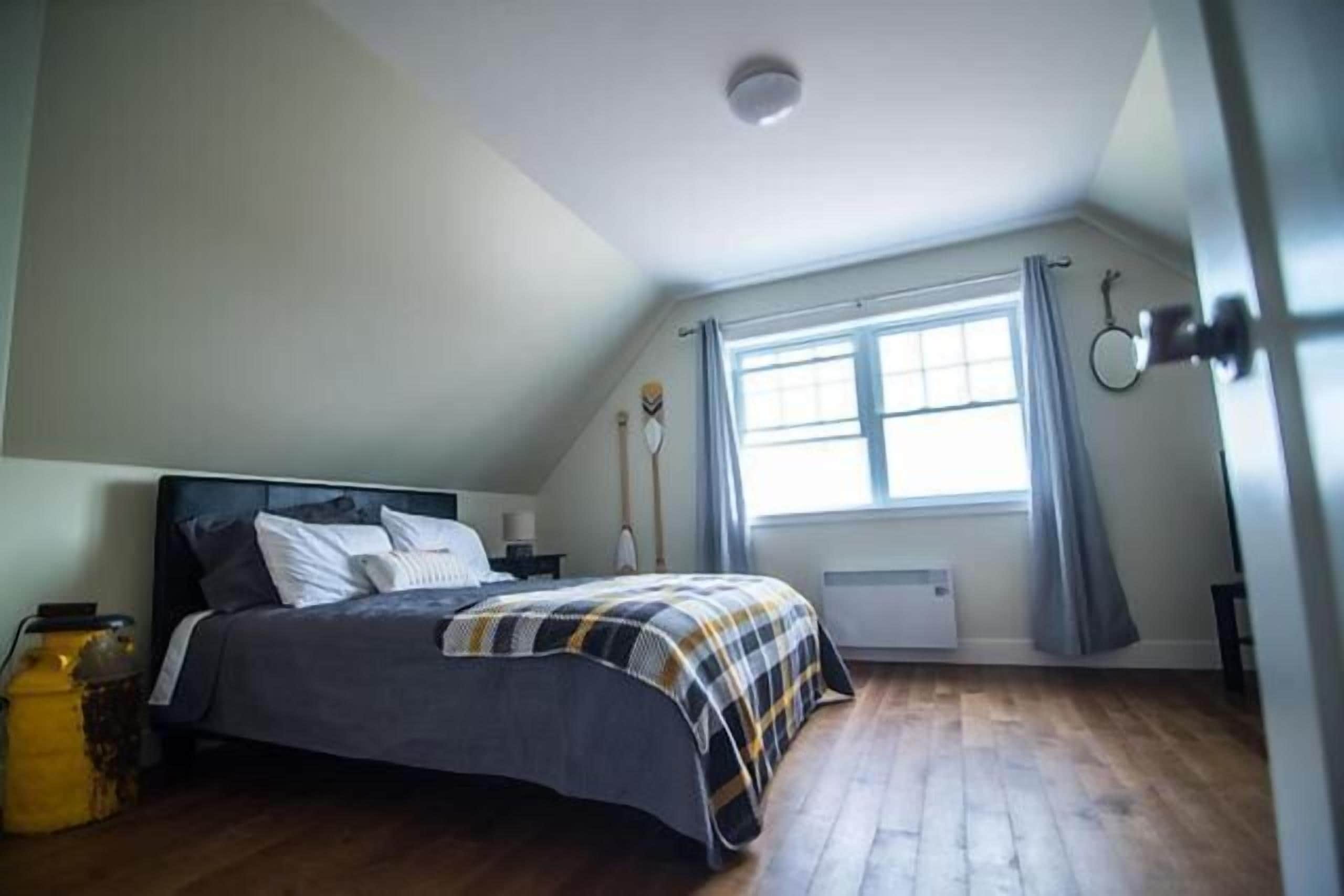 Un dormitorio con cama, ventana con cortinas, radiador y luz de techo.
