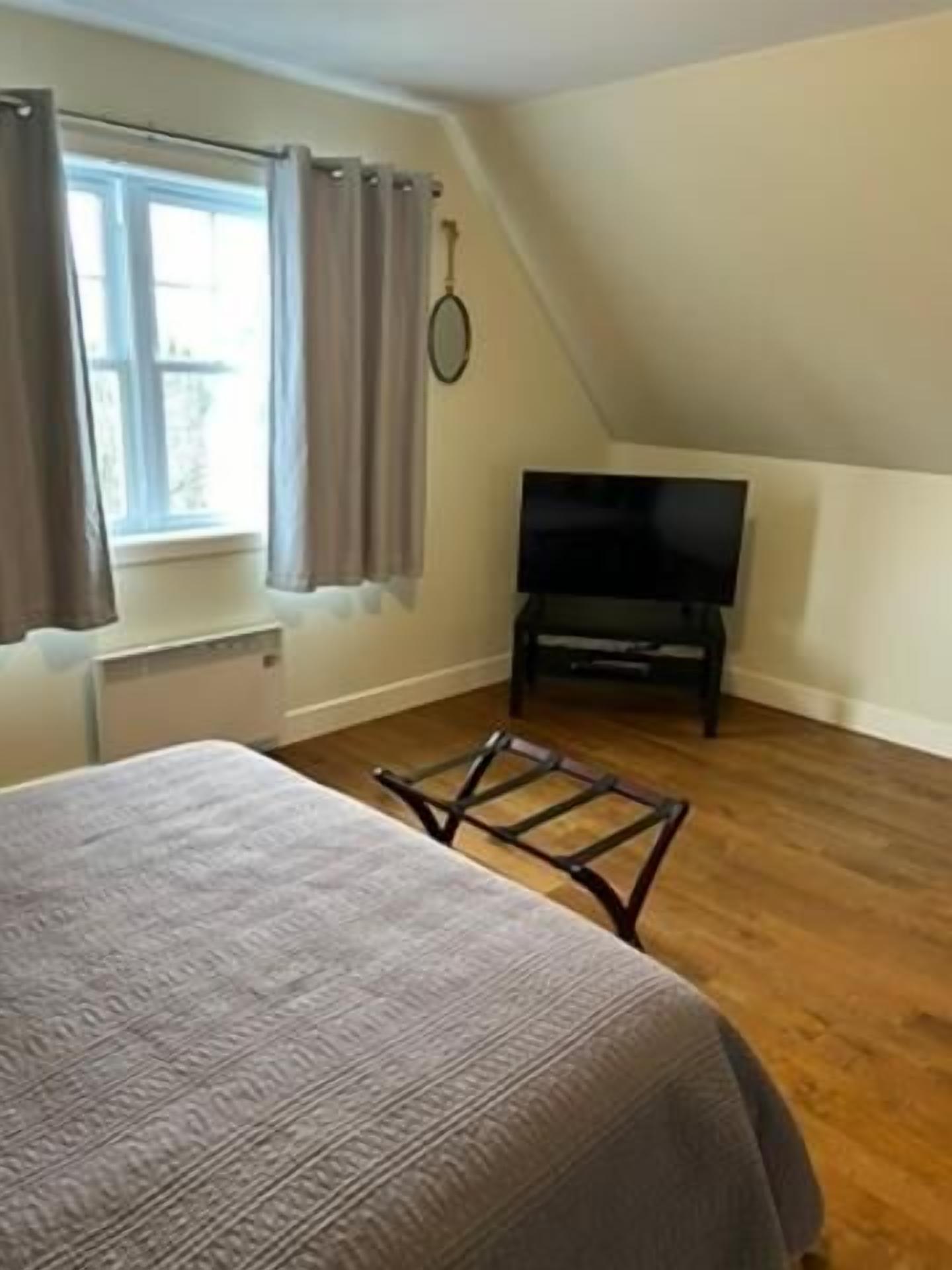 A bedroom with a bed, a television, and a window with curtains.