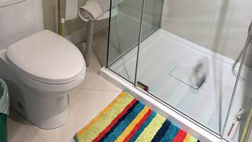 A bathroom with a glass shower enclosure, a toilet, and a roll of toilet paper on the wall.