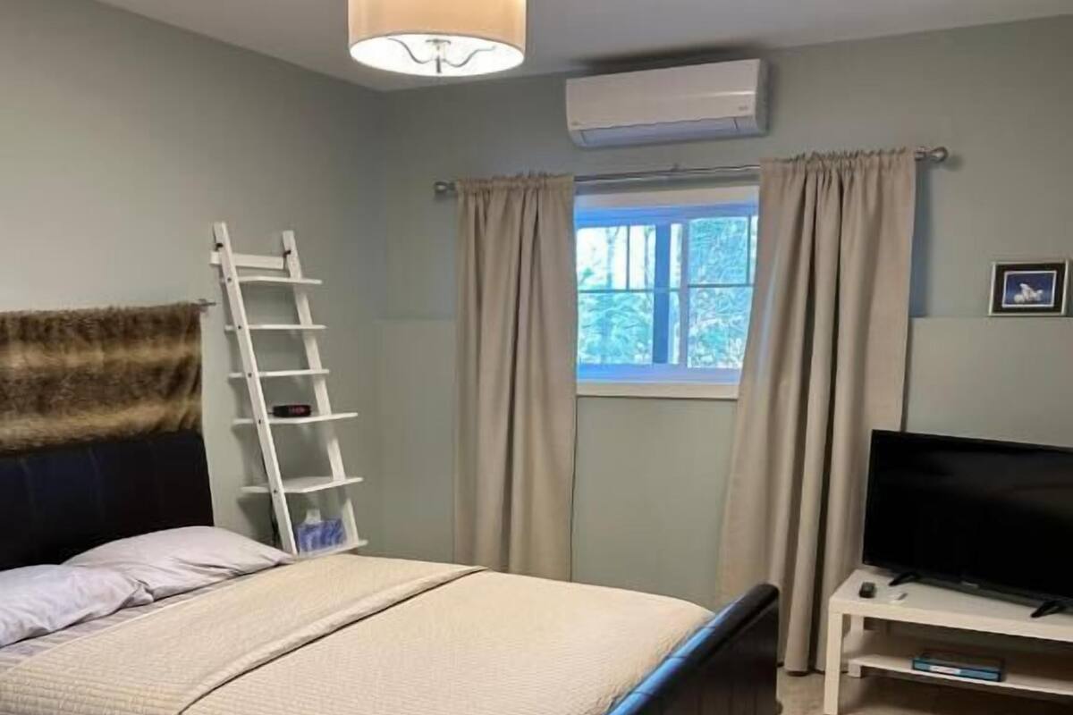 Een slaapkamer met een bed, een tv-meubel, een raam met gordijnen, een airconditioner en een plafondlamp.