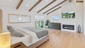 A modern bedroom with a bed, a fireplace, a TV, and a large window. - Silver Lake Hills Home with Views • Patio • Near Sunset Junction (Los Angeles)