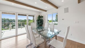 A modern dining area with a glass table and white chairs, large windows, and a view of greenery and buildings. - Silver Lake Hills Home with Views • Patio • Near Sunset Junction (Los Angeles)