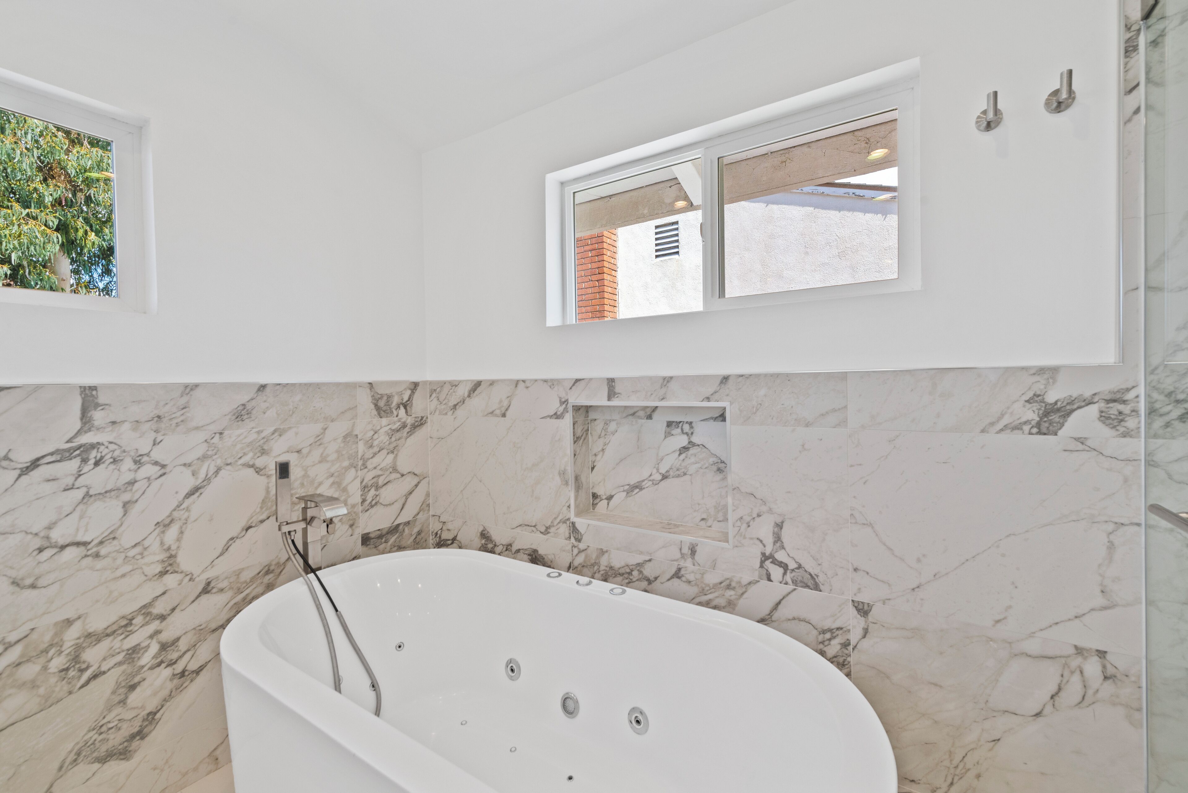 Un baño moderno con una bañera independiente, paredes de mármol y un ventanal con vistas al verdor.