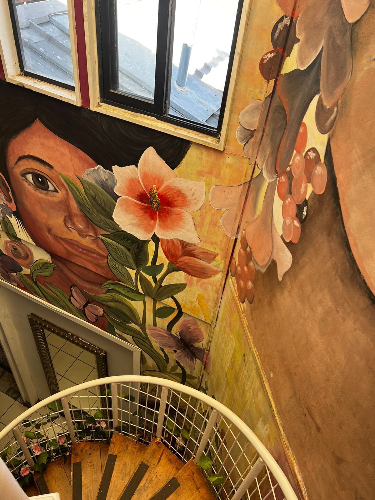 A staircase with a mural of a woman's face and flowers, a window, and a railing.