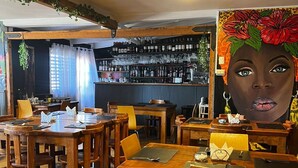 En restaurang med träbord och stolar, en bardisk med hyllor fulla av flaskor och en stor väggmålning på väggen.